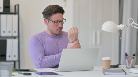 Middle Aged Man with Laptop having Wrist Pain in Officeの写真素材