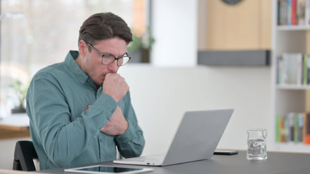 Middle Aged Man having Coughing while working on Laptopの写真素材