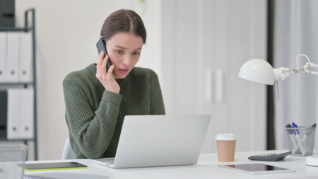 Young Woman with Laptop Talking on Smartphoneの写真素材