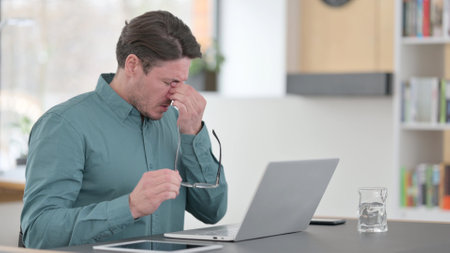 Middle Aged Man having Headache and Eyestrain while Working on Laptopの写真素材