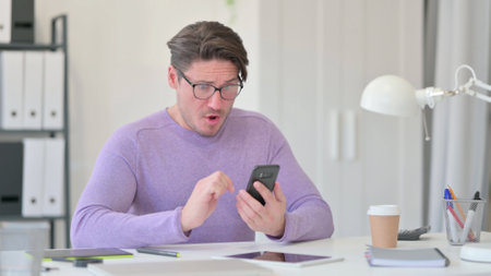 Middle Aged Man Shocked by Results on Smartphoneの写真素材
