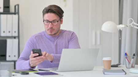 Middle Aged Man using Smartphone in Officeの写真素材