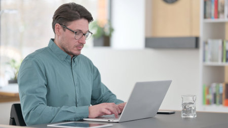 Middle Aged Man Working on Laptop in Officeの写真素材