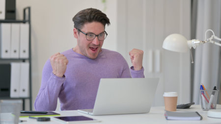 Middle Aged Man with Laptop Celebrating in Officeの写真素材