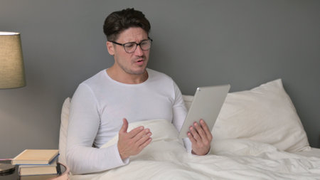 Middle Aged Man Reacting to Loss on Tablet in Bedの写真素材