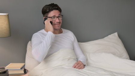 Middle Aged Man Talking on Smartphone in Bedの写真素材
