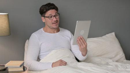 Online Video Chat on Tablet by Middle Aged Man in Bedの写真素材