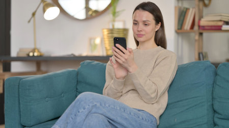 Young Woman using Smartphone on Sofaの写真素材