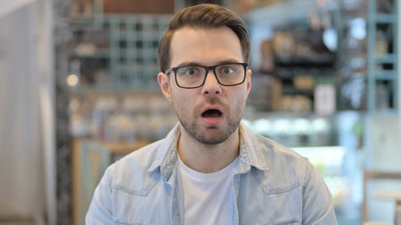 Portrait of Young Man Feeling Shocked in Cafeの写真素材