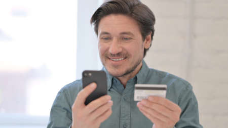 Portrait of Middle Aged Man with Successful Online Shopping on Smartphoneの写真素材