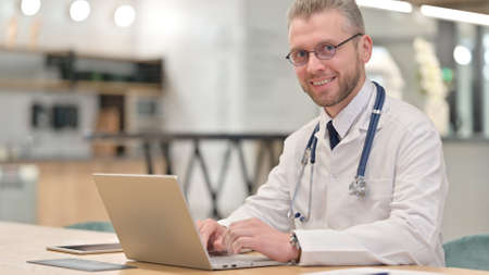 Cheerful Young Male Doctor with Laptop Looking at the Camera