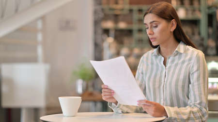 Serious Young Latin Woman Reading Documents in Cafe
