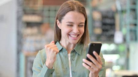 Excited Woman Cheering Success on Smartphoneの写真素材