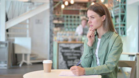 Woman Thinking and Writing on Paper in Cafe