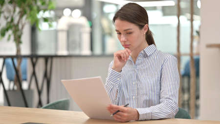 Pensive Young Woman Reading Documents in Office