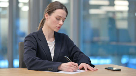 Young Businesswoman Writing on Paper in Officeの写真素材