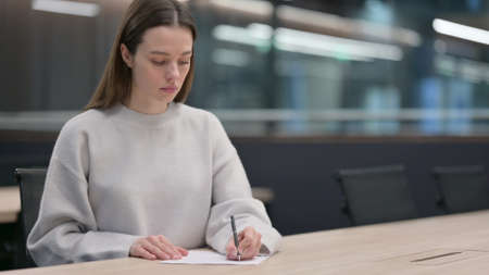 Attractive Woman Writing on Paper in Office