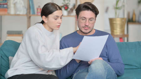 Young Mixed Race Couple Reading Documents Together on Sofaの写真素材