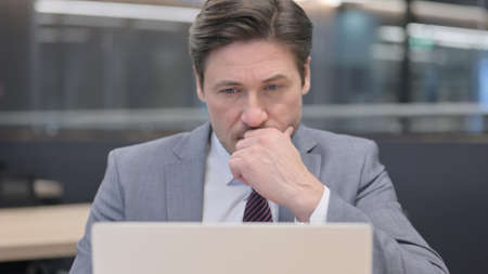 Pensive Middle Aged Businessman Thinking and Working on Laptopの写真素材