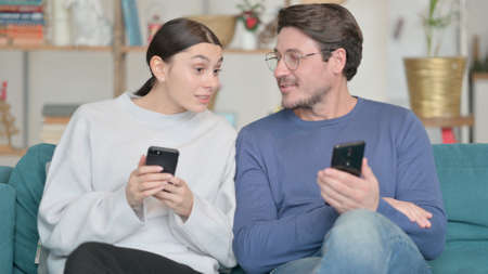 Mixed Race Couple using Smartphone and Talking While Sitting at Home