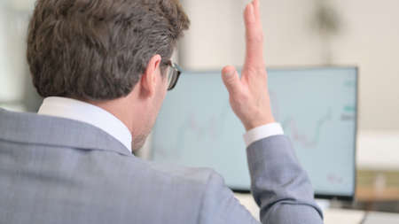 Businessman Celebrating while Reading Charts on Desktopの写真素材