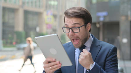 Young Businessman Celebrating on Tablet Outdoorの写真素材
