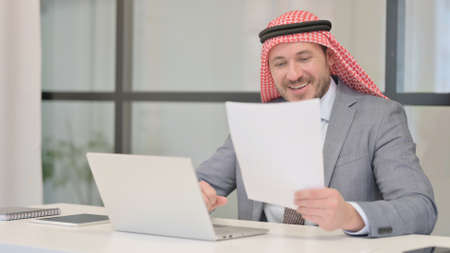 Arab Businessman with Laptop Reading Documentsの写真素材