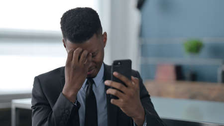 African Businessman Reacting to Loss on Smartphoneの写真素材
