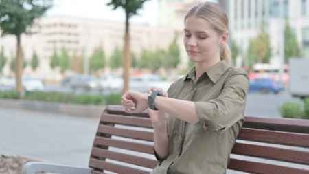 Woman Using Smartwatch while Sitting Outdoor on Benchの写真素材