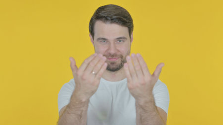 Young Man Inviting on Yellow Backgroundの写真素材