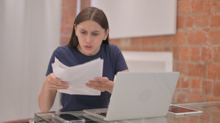 Young Latina Woman Shocked by Loss Report while Working on Laptopの写真素材