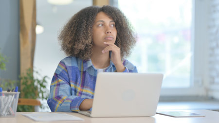 Young African Woman Thinking and Working on Laptop