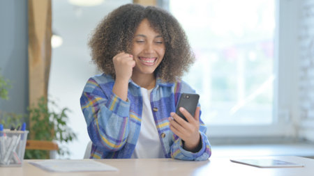 Young African Woman Celebrating Success on Smartphoneの写真素材