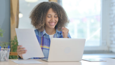 Young African Woman Celebrating Success with Laptop and Documents, Contract