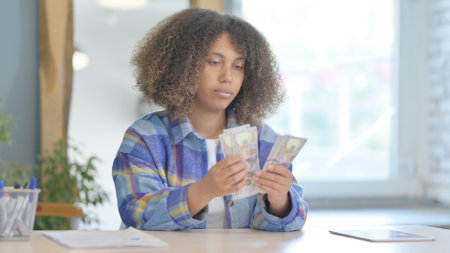 Young African Woman Counting Money while Sitting in Officeの写真素材