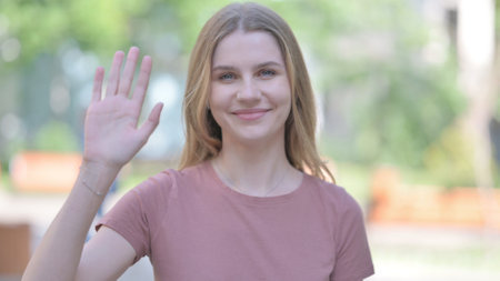 Outdoor Portrait of Young Woman Waving to Say Helloの写真素材