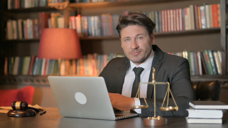 Serious Male Lawyer Looking at Camera while Working on Laptop