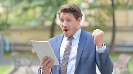 Businessman Celebrating on Tablet while Standing Outside Officeの写真素材