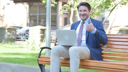 Thumbs Up by Middle Aged Businessman on Laptop Outdoorの写真素材