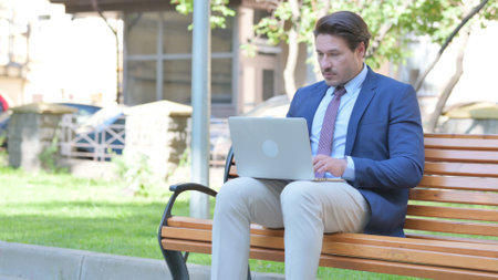 Middle Aged Businessman Working on Laptop Outdoorの写真素材