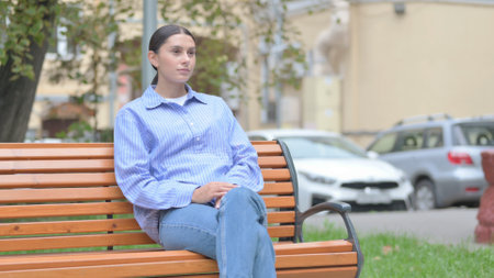 Serious Latin Woman Sitting Outdoor on Benchの写真素材