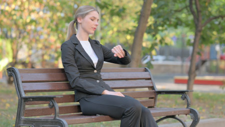 Waiting Businesswoman Checking Time on Wrist Watch while Sitting Outdoor on Benchの写真素材
