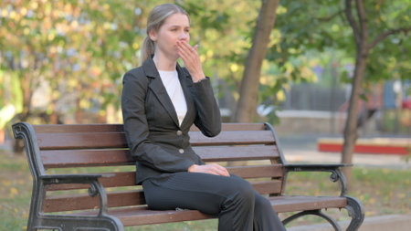 Sick Businesswoman Coughing while Sitting Outdoor on Benchの写真素材