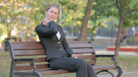 Businesswoman having Neck Pain while Sitting Outdoor on Benchの写真素材