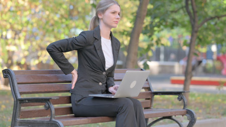 Businesswoman having Back Pain while Using Laptop Outdoorの写真素材