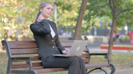 Businesswoman with Neck Pain Working on Laptop Outdoorの写真素材