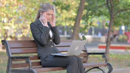 Businesswoman having Headache while Working on Laptop Outdoorの写真素材