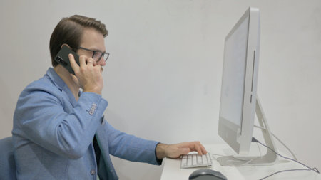 Middle Aged Man Talking on Phone while Working on Desktop