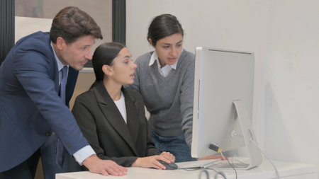 Hispanic Businesswoman Working on Computer with Teammatesの写真素材