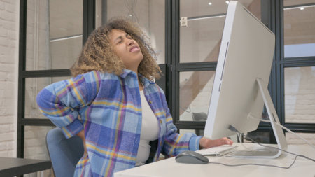 African Woman having Back Pain while Working on Desktopの写真素材